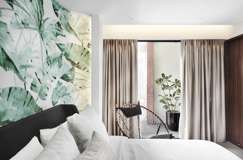 天花板的墙纸装饰主卧室的床头。设计师刻意暴露卧室阳台外的红砖墙，点出复古的热带风情。