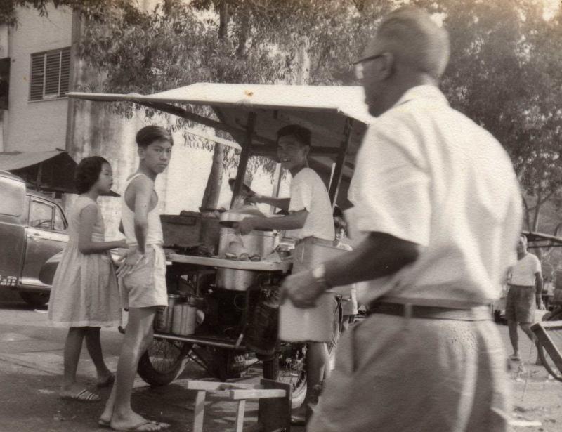 李三峇母亲1959年在街头卖水粿的流动摊子。图为李三峇的大哥在摊位帮忙。（受访者提供）