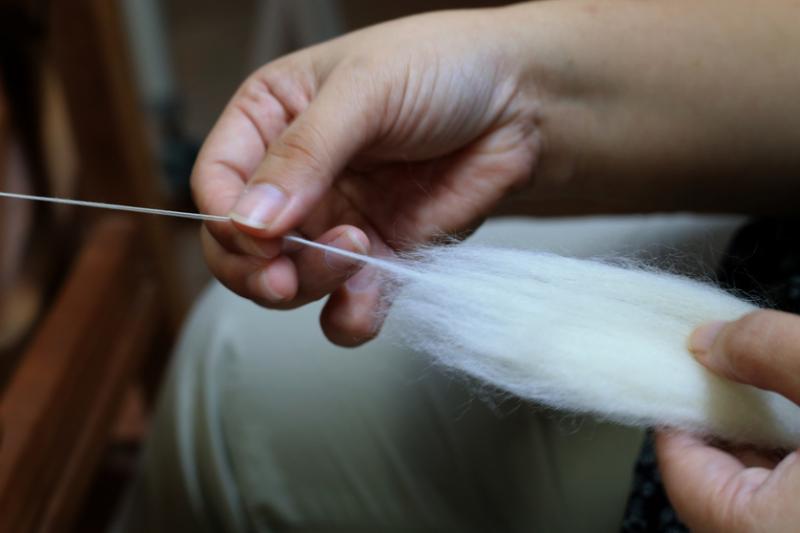 吴惠莲踩动脚踏板转动纺纱轮,将一团乱麻似的纤维拉伸加拈,扭成线。