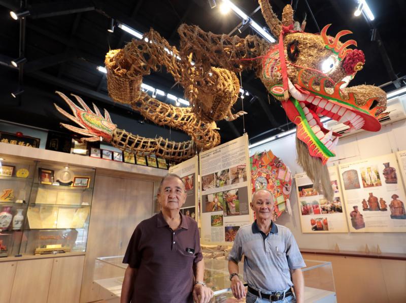 沙冈万山福德祠醒狮团敬称“龙王”的火龙顾问冯景源师傅（左）和醒狮团发起人之一的司徒根良，都已投身火龙制作40年。从妆艺大游行“退役”的稻草火龙高挂在沙冈古迹文物室内。（林国明摄）