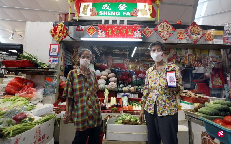 75岁的邓伈涞(右)和姐姐邓细妹在亚逸拉惹巴刹经营蔬菜摊位40多年,她去年学习使用手机后,也为摊位开通电子付费选项,下来希望通过翻译应用,学习简单英语同外国顾客沟通。(饶进礼摄) 75岁的邓伈涞(右)和姐姐邓细妹在亚逸拉惹巴刹经营蔬菜摊位40多年,她去年学习使用手机后,也为摊位开通电子付费选项,下来希望通过翻译应用,学习简单英语同外国顾客沟通。(饶进礼摄)