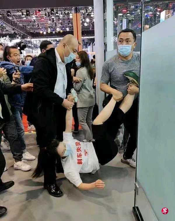 身穿印有“刹车失灵”字样白色T恤的女子,被车展两名保安强行拖出场外。(互联网) 身穿印有“刹车失灵”字样白色T恤的女子,被车展两名保安强行拖出场外。(互联网)