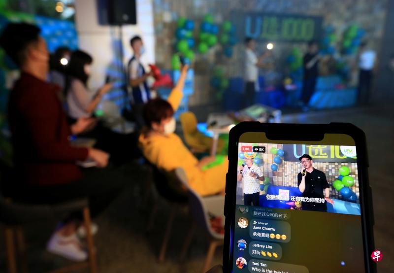 本地音乐人陈文华（手机屏幕，右）昨天傍晚到报业中心出席“U选1000”终极倒数活动，与UFM100.3全体DJ合唱冠军歌曲《刻在我心底的名字》。（龙国雄摄）