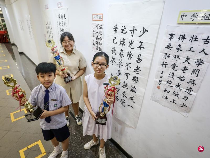第32届全国学生书法比赛小学组冠军鞠宇轩(左起)、高中组冠军易彦莹,以及中学组冠军黄相宜在新加坡书法中心领取奖杯,靠近镜头的三幅字分别出自他们之手。(严宣融摄) 第32届全国学生书法比赛小学组冠军鞠宇轩(左起)、高中组冠军易彦莹,以及中学组冠军黄相宜在新加坡书法中心领取奖杯,靠近镜头的三幅字分别出自他们之手。(严宣融摄)