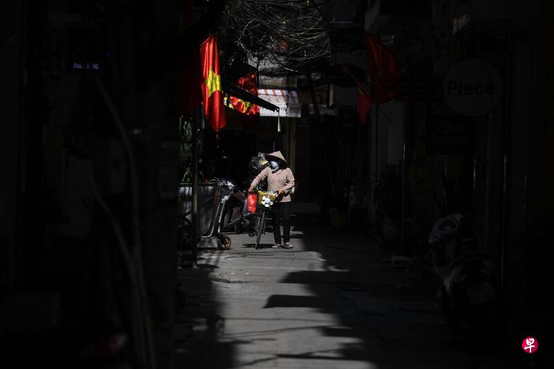 越南一名戴着口罩的妇女,推着一辆脚踏车走在首都河内一条街道上。(法新社) 越南一名戴着口罩的妇女,推着一辆脚踏车走在首都河内一条街道上。(法新社)