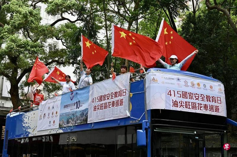 一辆宣传车星期一（4月15日）在香港油尖旺区巡游，车上人员挥舞国旗，宣传全民国家安全教育日。（中新社）