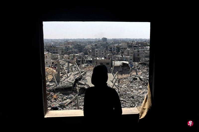 以色列过度打击加沙地带引发严重的人道主义危机，图为一名巴勒斯坦青年站着窗前遥望远处已成废墟的家园。（法新社）