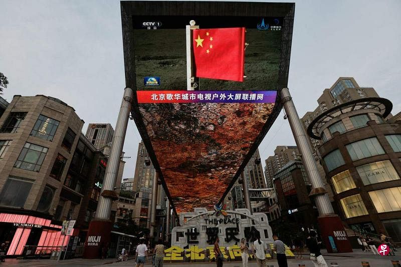 中国北京一个大屏幕星期二（6月4日）播映嫦娥六号在月球背面着陆后，五星红旗成功展开的新闻画面。（路透社）