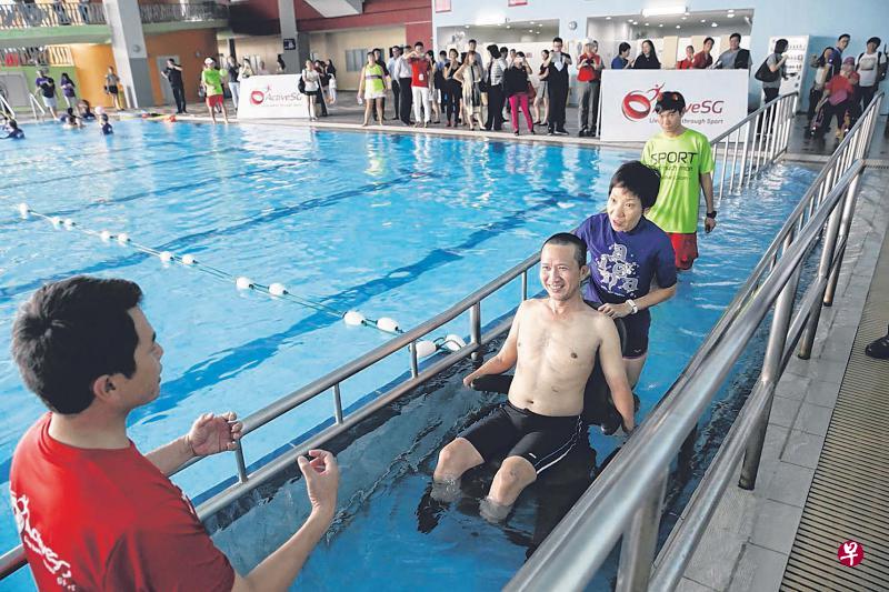 文社青部部长傅海燕(右二)推着轮椅,顺着残疾人入水通道将陈惠文(左二)送入泳池。(海峡时报) 文社青部部长傅海燕(右二)推着轮椅,顺着残疾人入水通道将陈惠文(左二)送入泳池。(海峡时报)