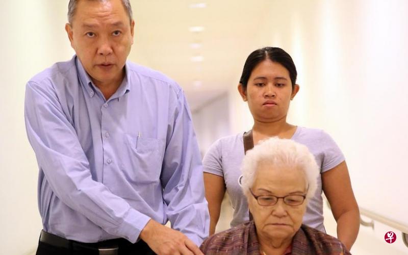 昇菘嬷刚动了胆囊手术,今早在儿子林福星(左)和女佣的陪同下,坐轮椅出庭。(《海峡时报》照片) 昇菘嬷刚动了胆囊手术,今早在儿子林福星(左)和女佣的陪同下,坐轮椅出庭。(《海峡时报》照片)