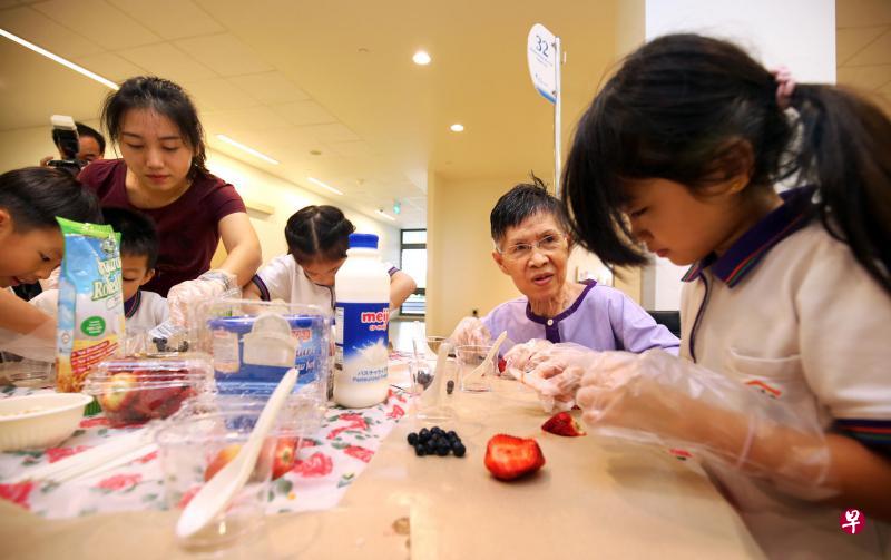 李丽娇(右二)与来自小小学庭托儿所的幼童一同制作水果酸奶,让她轻松度过一小时。这是义顺社区医院特别筹办的每周一次跨代活动。 李丽娇(右二)与来自小小学庭托儿所的幼童一同制作水果酸奶,让她轻松度过一小时。这是义顺社区医院特别筹办的每周一次跨代活动。