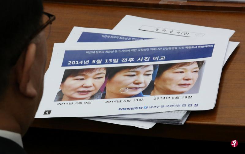 韩国一家整容医院的院长金荣宰14日在国会听证会上细看总统朴槿惠在5月9日、13日和19日拍摄的三张照片。(路透社) 韩国一家整容医院的院长金荣宰14日在国会听证会上细看总统朴槿惠在5月9日、13日和19日拍摄的三张照片。(路透社)