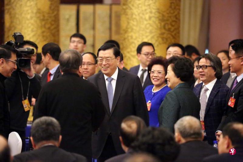 张德江（中）抵达会场后与港澳政协委员握手致意。（中通社）