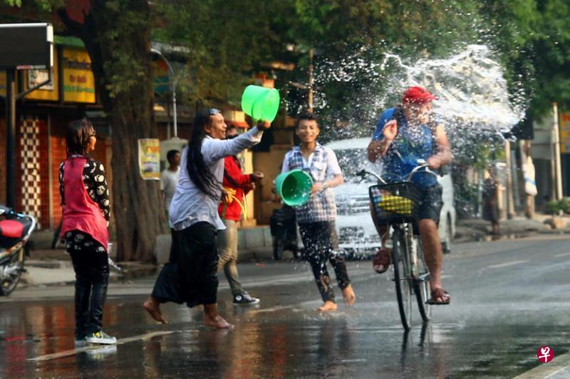 一名曼德勒居民热情地向路过的游客泼水。 一名曼德勒居民热情地向路过的游客泼水。