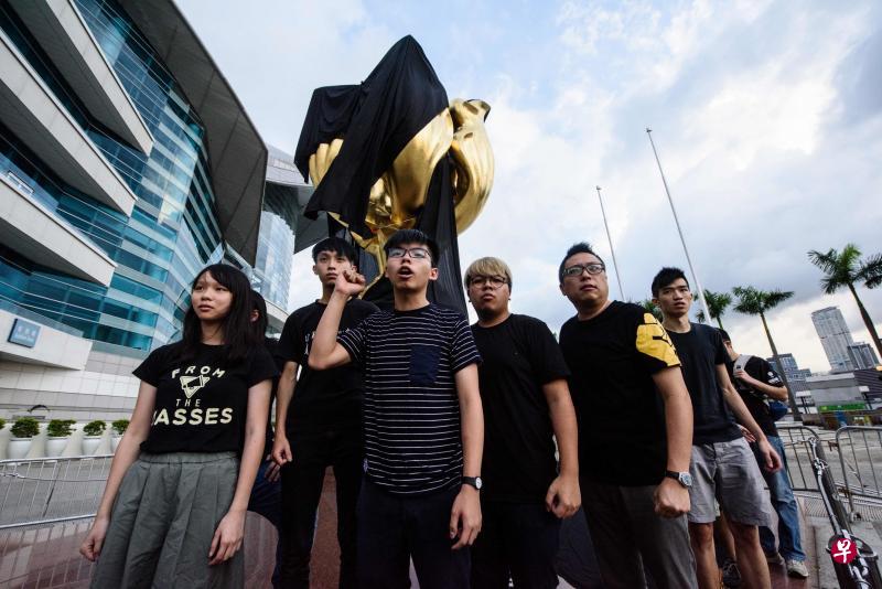 香港众志秘书长黄之锋(左三),连同该党成员,以及社民连和人民力量组织的10人,昨天清场到湾仔金紫荆广场,以黑布包裹广场上的紫荆花雕塑,抗议中央政府没有落实“一国两制”。(法新社) 香港众志秘书长黄之锋(左三),连同该党成员,以及社民连和人民力量组织的10人,昨天清场到湾仔金紫荆广场,以黑布包裹广场上的紫荆花雕塑,抗议中央政府没有落实“一国两制”。(法新社)