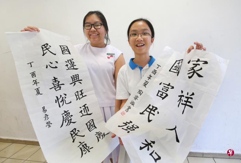 易彦莹（左）和陶姿璇挥毫为新加坡建国52周年献上美好祝愿，她们分别获得本届全国中小学生书法比赛中学组和小学组的冠军。（陈福洲摄）