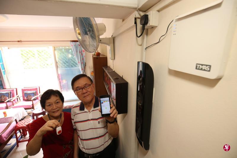徐熊刚(右)及妻子洪亚菊在家里安装年长者智慧看护系统,右上角为系统的主机。洪亚菊随身携带紧急呼救按钮,徐熊刚可从手机查看传感器记录的数据。(邝启聪摄) 徐熊刚(右)及妻子洪亚菊在家里安装年长者智慧看护系统,右上角为系统的主机。洪亚菊随身携带紧急呼救按钮,徐熊刚可从手机查看传感器记录的数据。(邝启聪摄)