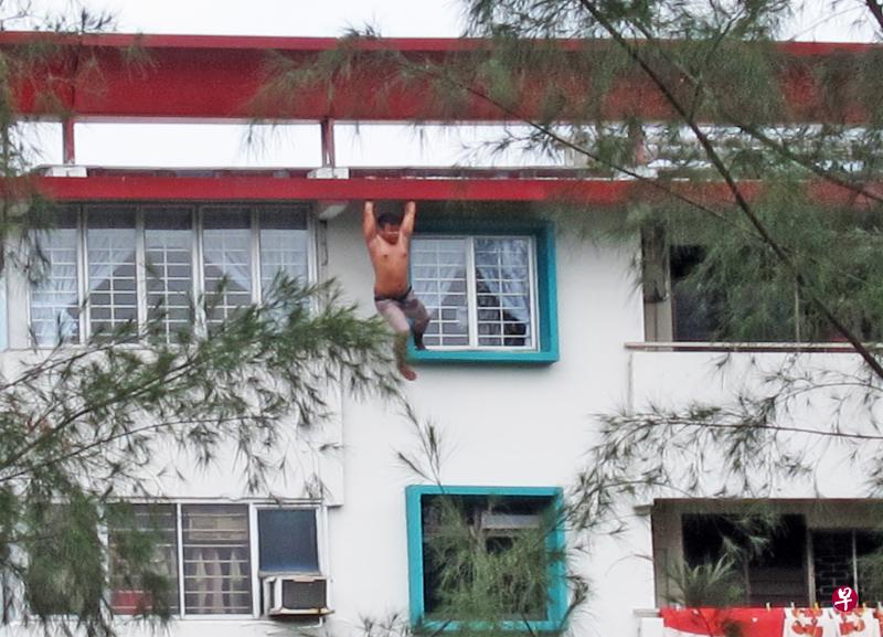 男子双手紧握屋檐铁柱,不时甩动身体。 男子双手紧握屋檐铁柱,不时甩动身体。