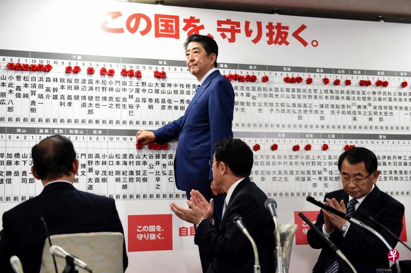 日本首相安倍在东京自民党总部的当选议员榜上钉上小红花。(法新社) 日本首相安倍在东京自民党总部的当选议员榜上钉上小红花。(法新社)