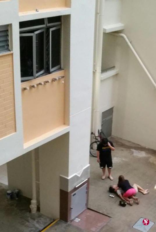 男子倒卧组屋楼下，相信是他母亲的一名妇女跪在身旁抱住他。（读者提供）