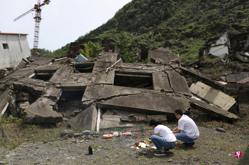北川老县城里，一对年轻夫妇在废墟前祭奠在地震中逝去的亲人。（新华社）