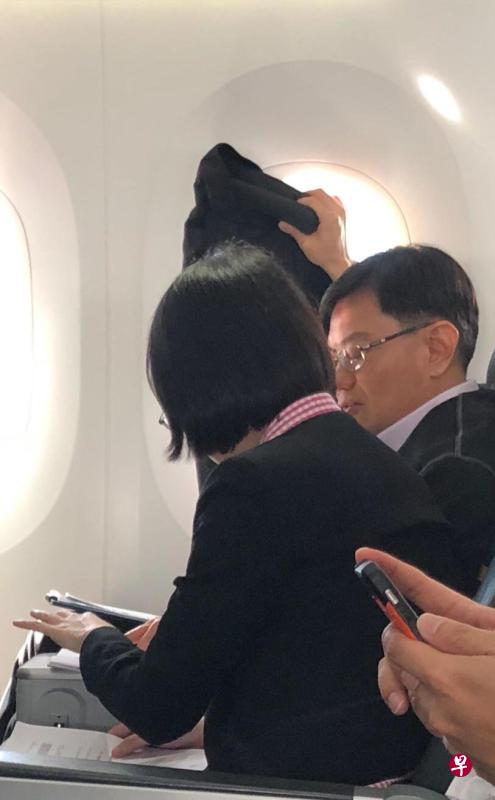 王瑞杰在机舱里跟下属讨论工作，还自己用西装挡住窗外的强光。（乘客提供）