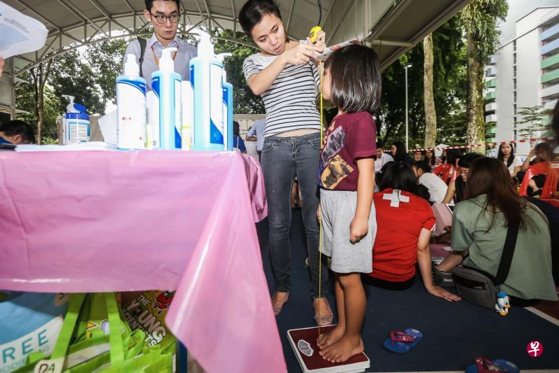 幼儿培育署和淡马锡关怀基金资助的“邻里儿童保健服务”，过去两天在文礼通道举办以弱势孩童为对象的社区体检活动。图为现场的大学生义工为孩童量体重和身高。（梁伟康摄）