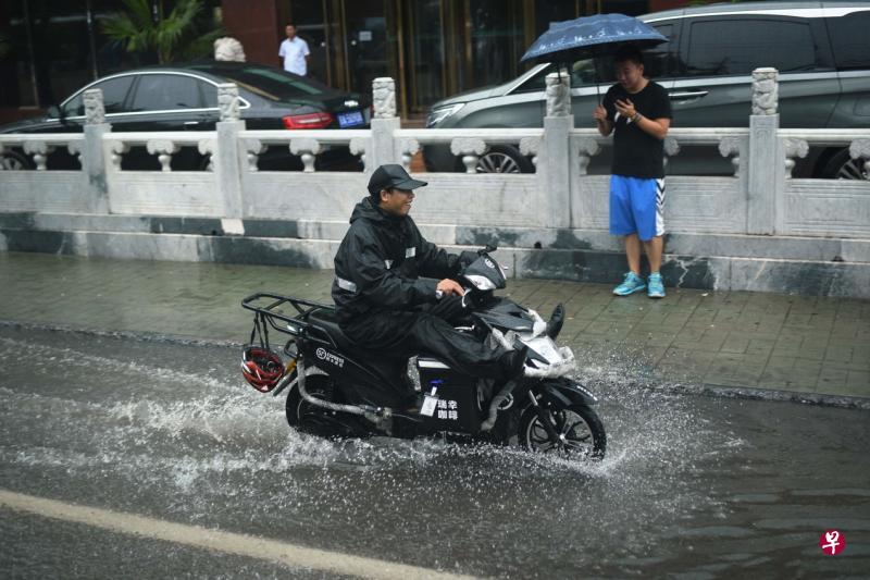 北京昨天持续降雨天气，图为一名市民骑车经过积水街道时提起双腿。（法新社）