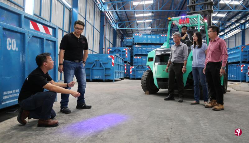 两名来自MOVeS的专员(黑衣者),向张致源(右起)、张少瑱、张木山和叉车司机(坐叉车上)讲解叉车提示灯的用途。(梁麒麟摄) 两名来自MOVeS的专员(黑衣者),向张致源(右起)、张少瑱、张木山和叉车司机(坐叉车上)讲解叉车提示灯的用途。(梁麒麟摄)