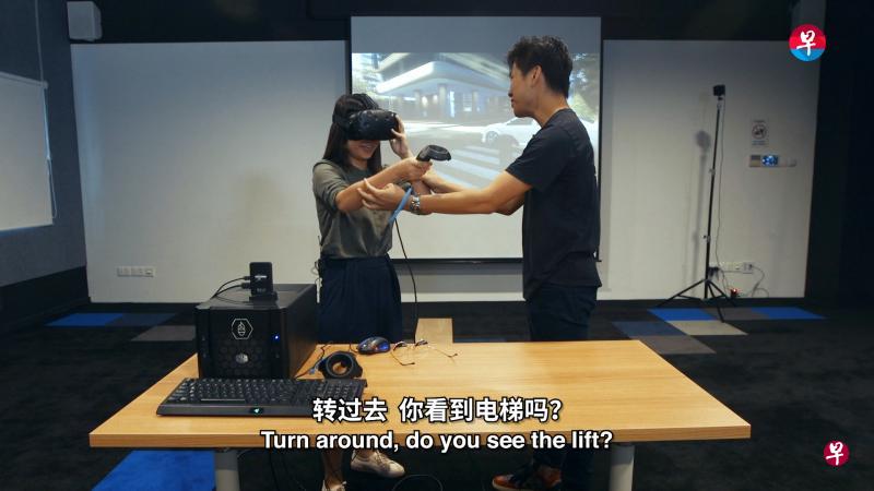 华文媒体集团新闻中心记者卓彦薇(左)在虚拟实境体验设计师丘勇凯(右)的指导下,体验虚拟实境游戏“Richies Plank”,“走进”电梯,感受高空俯瞰的特殊体验。(视频截图) 华文媒体集团新闻中心记者卓彦薇(左)在虚拟实境体验设计师丘勇凯(右)的指导下,体验虚拟实境游戏“Richies Plank”,“走进”电梯,感受高空俯瞰的特殊体验。(视频截图)