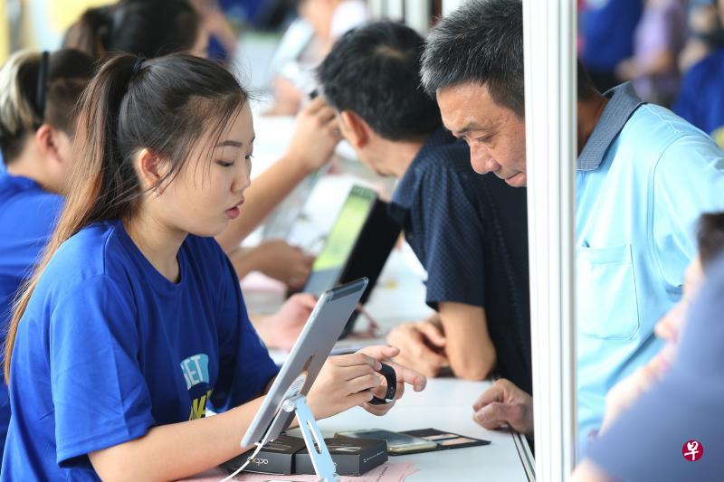 全国健步大挑战吸引大批公众报名参加，工作人员向公众解释运动手环的操作方法。（梁伟康摄）