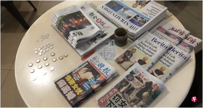 桌子上摆有六种报纸,旁边则备有零钱给顾客自行找钱。 桌子上摆有六种报纸,旁边则备有零钱给顾客自行找钱。