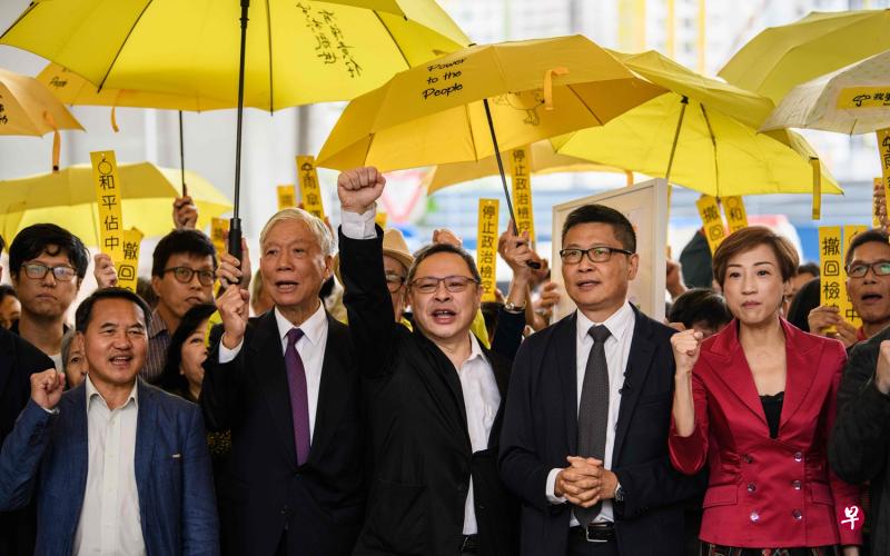 “占中三子”(前排左二起)朱耀明、戴耀廷与陈健民昨天出庭前和一众支持者在西九龙裁判法院外喊口号。(法新社) “占中三子”(前排左二起)朱耀明、戴耀廷与陈健民昨天出庭前和一众支持者在西九龙裁判法院外喊口号。(法新社)