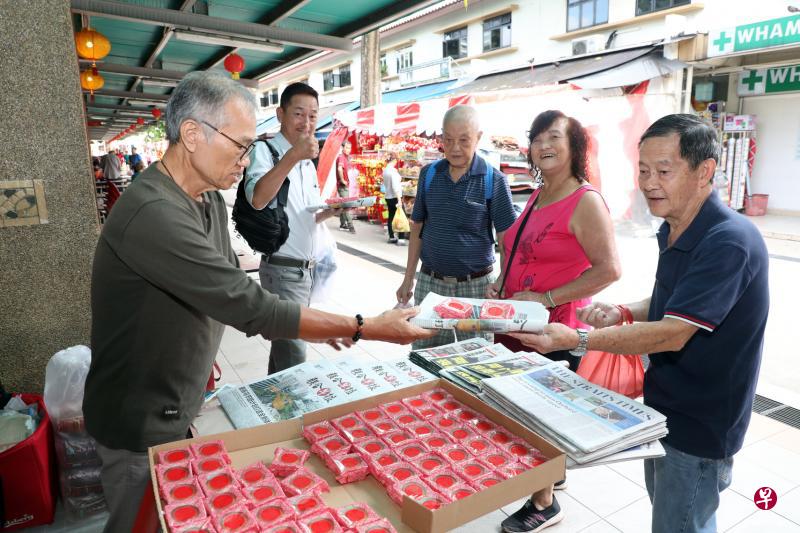 报贩何昱菘(左一)把一份《联合早报》和两颗五谷丰黄梨挞递给忠实读者陈民照。(邝启聪摄) 报贩何昱菘(左一)把一份《联合早报》和两颗五谷丰黄梨挞递给忠实读者陈民照。(邝启聪摄)