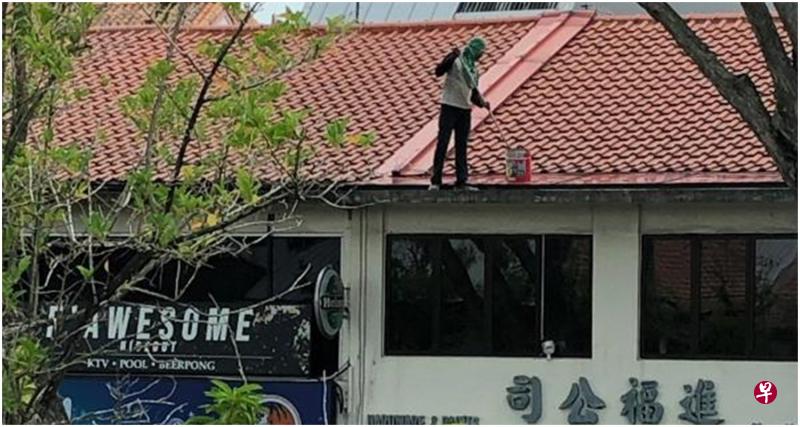 男子一手握刷子,一手提油漆桶,在两层楼店屋的屋顶上来回走动粉刷,对面顾客看得胆战心惊。(受访者提供) 男子一手握刷子,一手提油漆桶,在两层楼店屋的屋顶上来回走动粉刷,对面顾客看得胆战心惊。(受访者提供)