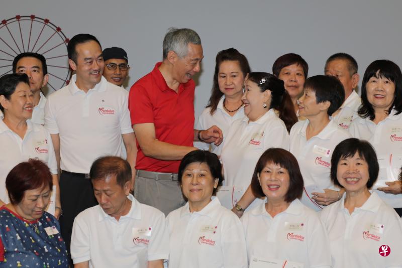 李显龙总理(穿红衣者)与多名和他一样,在昨天(6月2日)领取立国一代福利包的居民合影,其中包括他致辞时提到的黄亚兰(中排右三)。在总理右边的是同为宏茂桥集选区议员、贸工部高级政务部长许宝琨医生。(林国明摄) 李显龙总理(穿红衣者)与多名和他一样,在昨天(6月2日)领取立国一代福利包的居民合影,其中包括他致辞时提到的黄亚兰(中排右三)。在总理右边的是同为宏茂桥集选区议员、贸工部高级政务部长许宝琨医生。(林国明摄)