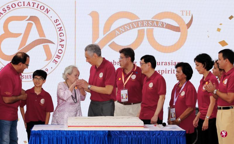 与欧亚裔协会同岁的退休护士长菲莉丝(左三)在切蛋糕仪式上亲吻了李显龙总理(左四)的右手,感谢他出席欧亚裔协会百年大庆庆典。在台上的还有部长易华仁(左起)、去年小六离校考试“欧亚裔状元”特雷、欧亚裔协会会长亚历西斯博士、副总理王瑞杰、协会义工慧拉瑞、议员祖安清心、舞蹈员萨曼莎,以及议员迪舒沙。(梁麒麟摄) 与欧亚裔协会同岁的退休护士长菲莉丝(左三)在切蛋糕仪式上亲吻了李显龙总理(左四)的右手,感谢他出席欧亚裔协会百年大庆庆典。在台上的还有部长易华仁(左起)、去年小六离校考试“欧亚裔状元”特雷、欧亚裔协会会长亚历西斯博士、副总理王瑞杰、协会义工慧拉瑞、议员祖安清心、舞蹈员萨曼莎,以及议员迪舒沙。(梁麒麟摄)