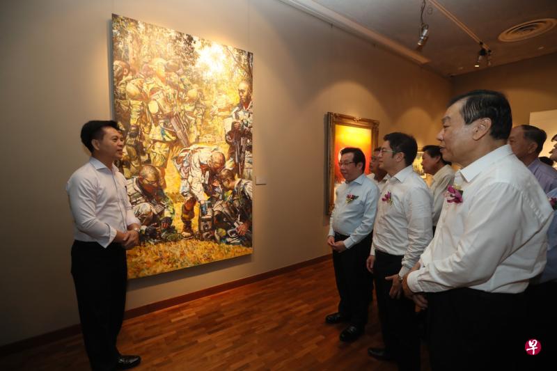 第10届“义安国庆书画美展”开幕，画家范少华向义安公司副义务财政兼义安文化小组委员会主任谢楚明（右起）、义安公司总理张绵耀、义安公司义务财政张伟伟，介绍他于2017年在德光岛绘制的作品《烈日德光岛》。（吴伟国摄）
