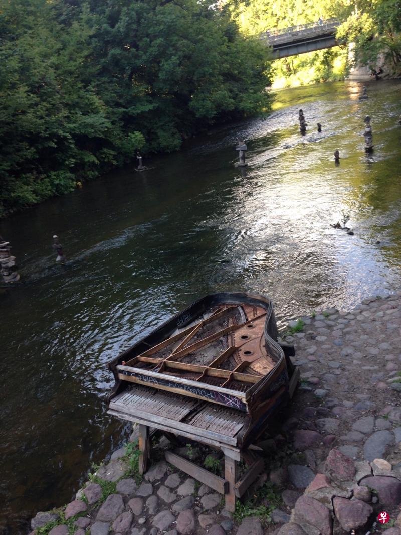 奥苏比斯艺文区为维尔尼亚河环绕,废弃的钢琴与河中石雕相对望。(黄向京摄) 奥苏比斯艺文区为维尔尼亚河环绕,废弃的钢琴与河中石雕相对望。(黄向京摄)