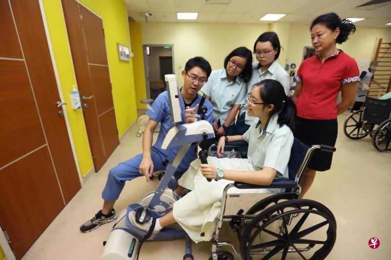 “医疗行业导师计划”让崇文中学的学生跟班向医疗从业员学习。图为物理治疗师黄聿勋(左一)向学生陈彦霖(试用器材者)、黄静雯和陈蕙昕(后排左一和二),讲解病人如何利用踏板式训练器进行复健。崇文中学咨询委员会成员王伟玲在一旁聆听。(林明顺摄) “医疗行业导师计划”让崇文中学的学生跟班向医疗从业员学习。图为物理治疗师黄聿勋(左一)向学生陈彦霖(试用器材者)、黄静雯和陈蕙昕(后排左一和二),讲解病人如何利用踏板式训练器进行复健。崇文中学咨询委员会成员王伟玲在一旁聆听。(林明顺摄)