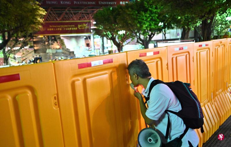 香港警方昨天正式解封被围堵近两周的香港理工大学。图为一名手持扩音器的男子透过理大校园外的水马缝隙窥探校园内部。(法新社) 香港警方昨天正式解封被围堵近两周的香港理工大学。图为一名手持扩音器的男子透过理大校园外的水马缝隙窥探校园内部。(法新社)