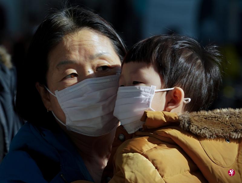 在韩国首尔街头，一名妇人抱着幼儿外出，两人都戴着口罩。（路透社） 