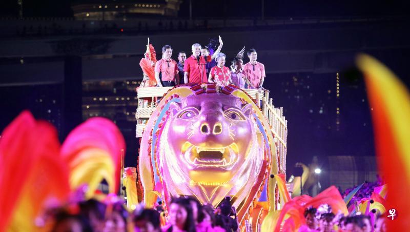 李显龙总理和夫人何晶(花车上左三和四)昨晚乘坐鱼尾狮花车驶入FI维修大楼,为妆艺首场演出掀开序幕。陪同李总理伉俪出席活动的包括贸工部长陈振声(左二)和人协总执行理事长陈国明(右一)。(林泽锐摄) 李显龙总理和夫人何晶(花车上左三和四)昨晚乘坐鱼尾狮花车驶入FI维修大楼,为妆艺首场演出掀开序幕。陪同李总理伉俪出席活动的包括贸工部长陈振声(左二)和人协总执行理事长陈国明(右一)。(林泽锐摄)