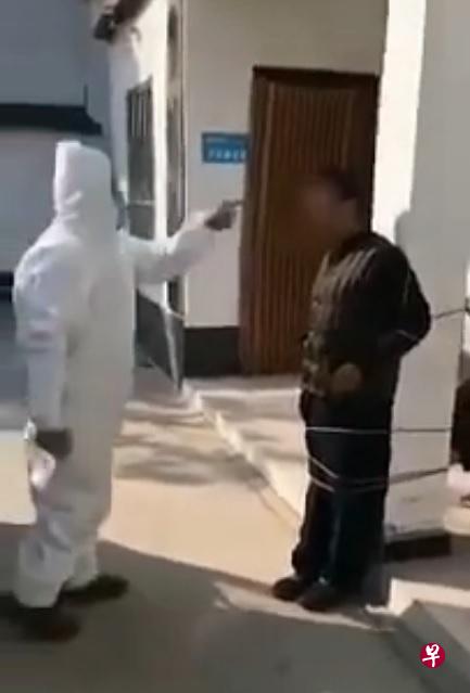 网传视频显示,河南一名村民(右)因不戴口罩被捆绑在墙柱上,并被一名穿着白色防护套的人员斥责。(视频截图) 网传视频显示,河南一名村民(右)因不戴口罩被捆绑在墙柱上,并被一名穿着白色防护套的人员斥责。(视频截图)