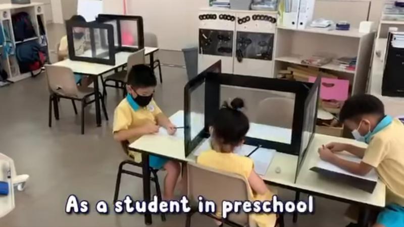 社会及家庭发展部长李智陞在面簿上分享视频，显示孩童如何学习遵守幼儿培育署的安全复课措施。图为一所学前中心的孩童在装有塑料防护屏的桌上学习。（取自李智陞面簿）