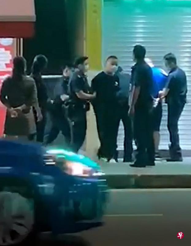 身穿蓝衣的前火锅店老板和一名黑衣男子双手被拷，押上警车。（受访者提供）