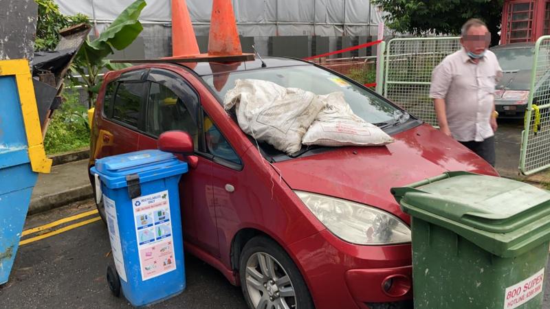目击者说,阿叔发现门前停放红色轿车时,搬起路边两个交通锥,和两袋沙包放到红色轿车的车顶。(受访者提供) 目击者说,阿叔发现门前停放红色轿车时,搬起路边两个交通锥,和两袋沙包放到红色轿车的车顶。(受访者提供)