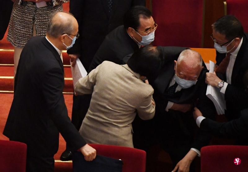 昨天的全国人大开幕式结束,董建华在离开座位时突然跌倒,旁边的与会代表连忙上前搀扶。(法新社) 昨天的全国人大开幕式结束,董建华在离开座位时突然跌倒,旁边的与会代表连忙上前搀扶。(法新社)
